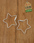 Pair of silver wire star-shaped hoop earrings on a wooden surface