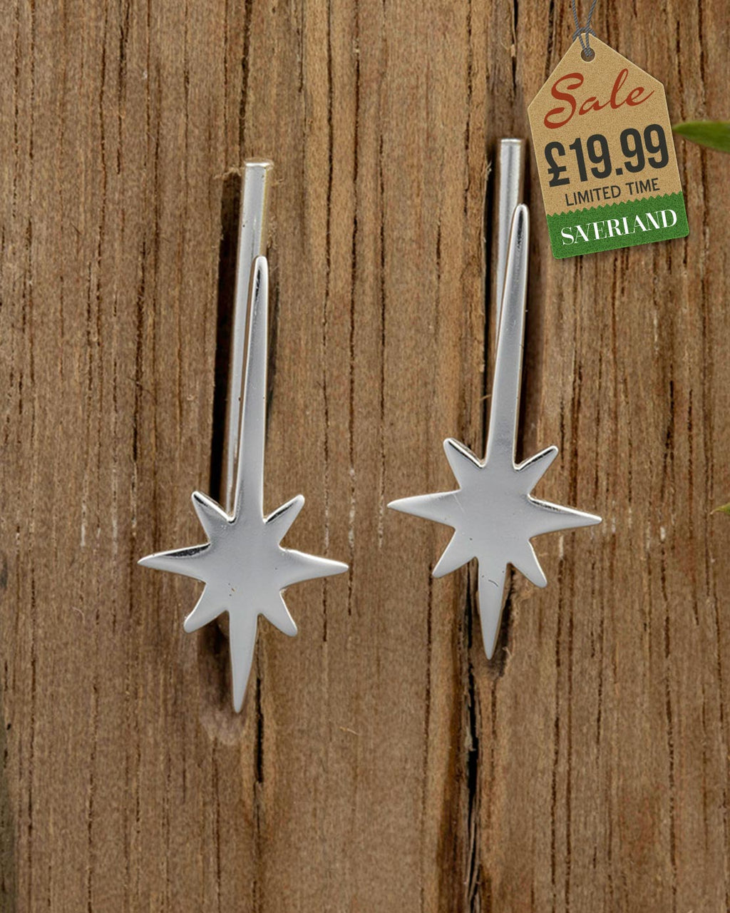 Pair of silver shooting star drop earrings with eight-pointed star charm and bar drop on wooden background