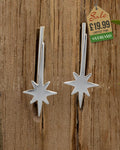 Pair of silver shooting star drop earrings with eight-pointed star charm and bar drop on wooden background