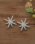 Silver-tone eight-pointed starburst stud earrings pavé set with cubic zirconia crystals on a wooden surface