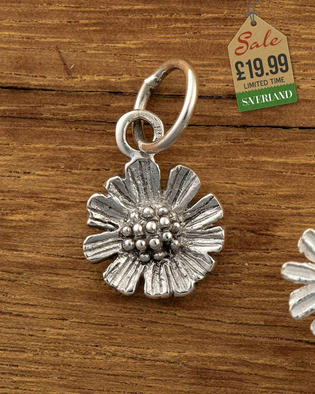 Silver-tone antique finish flower charm pendant with beaded centre and jump ring on wooden background