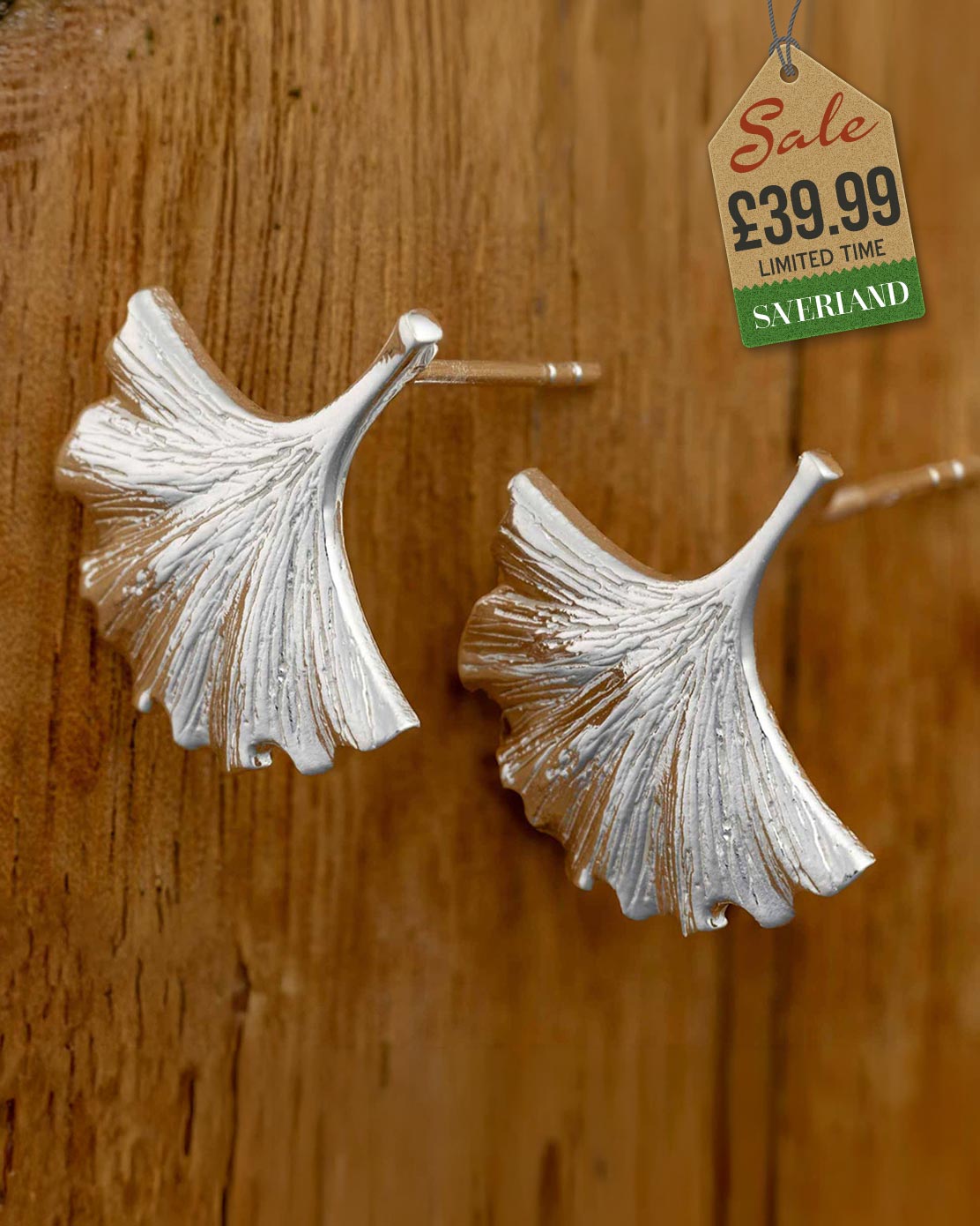 Pair of silver ginkgo leaf stud earrings with textured vein detail displayed on a wooden surface