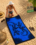 Woman laying out a royal blue and black tribal gecko beach towel on sand at beach
