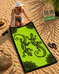 Woman laying out a lime green and black tribal gecko beach towel on sand at beach