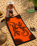 Woman laying out a orange and black tribal gecko beach towel on sand at beach