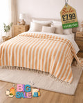 Orange and white striped throw blanket with tassel fringe draped over a bed in a bright bedroom