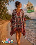 Woman wearing a vibrant boho paisley print kaftan beach cover-up in burgundy and teal walking on a tropical beach