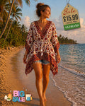 Woman wearing a white boho floral kaftan top with red and gold print, drawstring waist and tassel, walking on a tropical beach