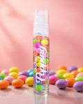 DDonna Popping Sweet Lip Oil pump bottle filled with colourful candy beads surrounded by multicoloured sweets on a pink background