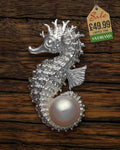 Silver-tone seahorse pendant with large lustrous pearl set in curled tail on wooden background
