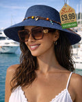 Woman wearing tortoise shell oversized sunglasses with gold logo accent at marina with navy straw hat