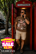 Man wearing a brown graphic t-shirt with Manitoba Social collage print, standing in a red British telephone box