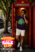 Man wearing a navy blue t-shirt with green and white 'The Energy Is About To Shift' slogan graphic, standing in a red British telephone box