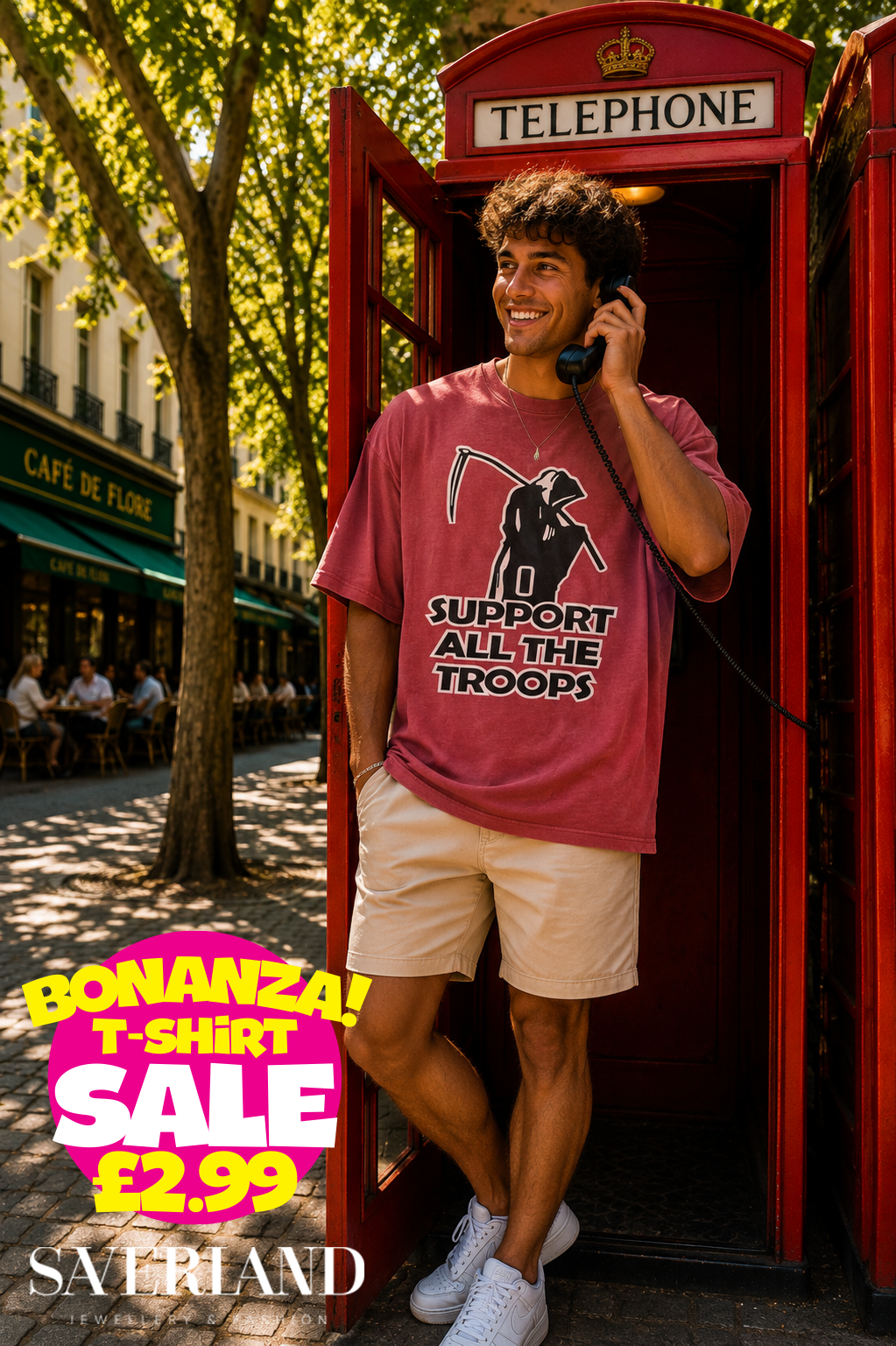 Man wearing a washed burgundy oversized t-shirt with a Grim Reaper graphic and 'Support All The Troops' slogan, standing in a red telephone box