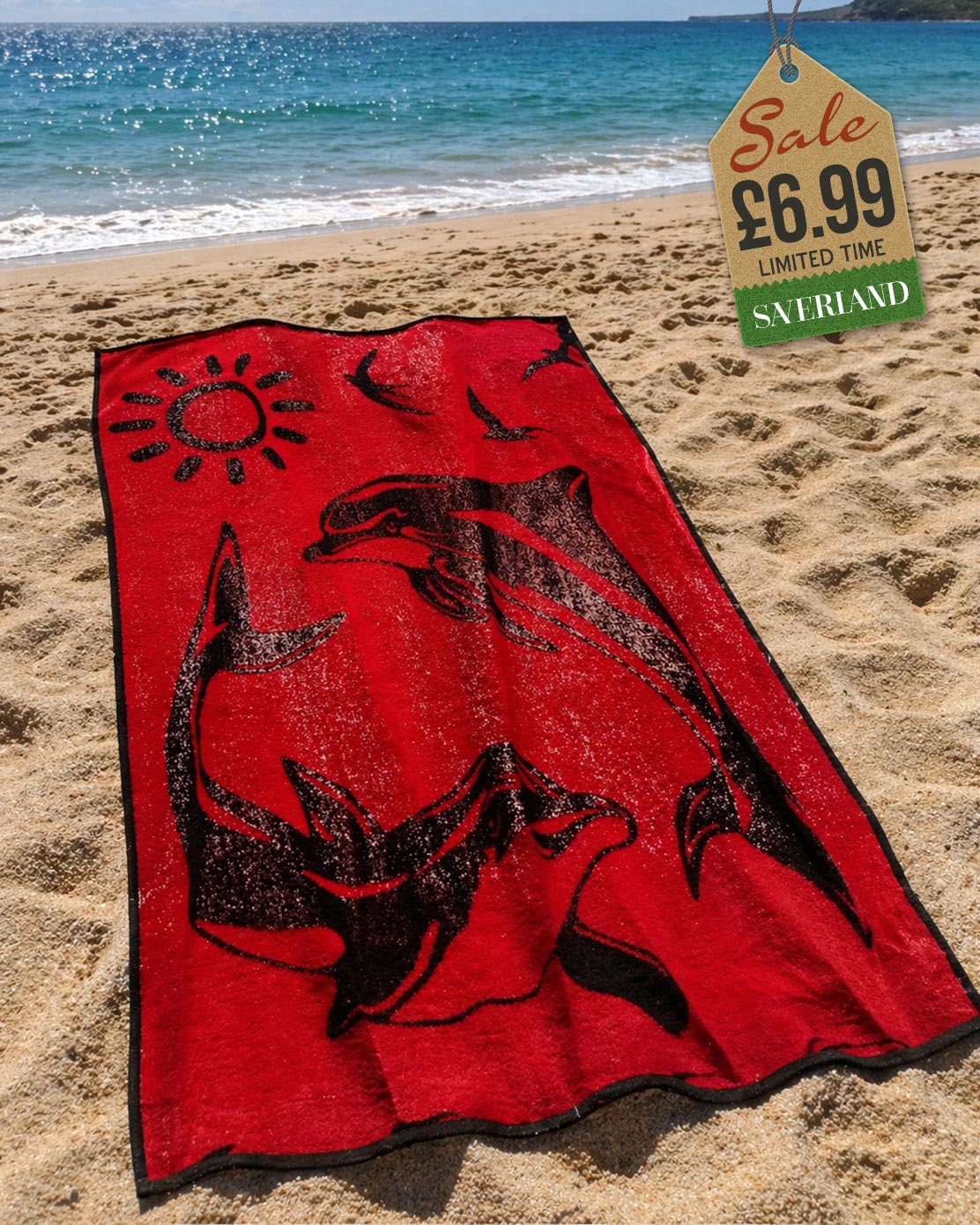 Red beach towel with black dolphin and sun print design laid out on sandy beach